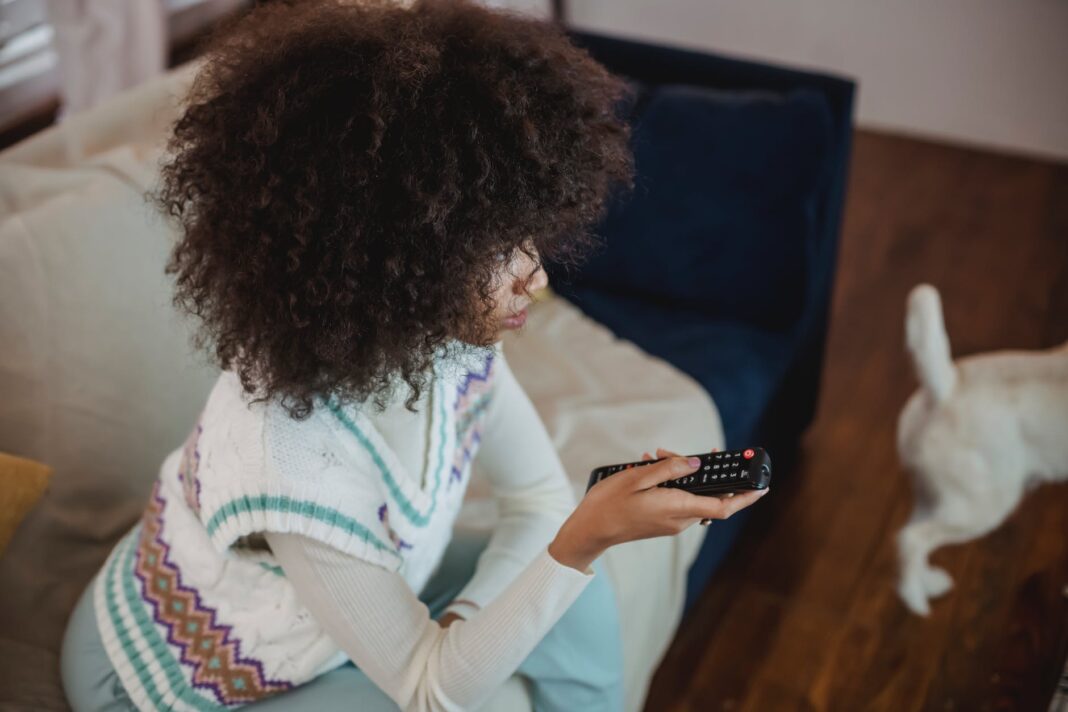 concentrated young african american lady switching tv channels while recreating on couch